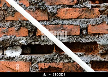 A weathered, textured red brick wall with visible mortar and some missing bricks, showcasing an aged and rustic architectural background. Stock Photo