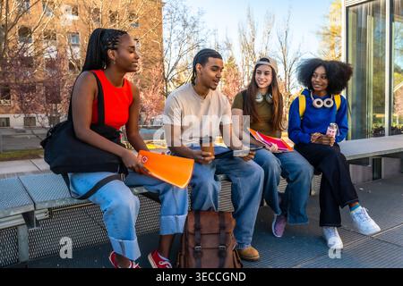 Diverse students talking on university campus bench Stock Photo