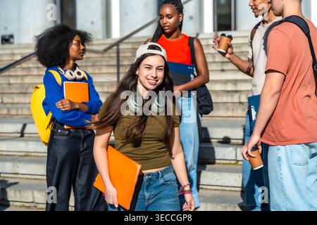 Diverse students walking, talking, and smiling on university campus Stock Photo