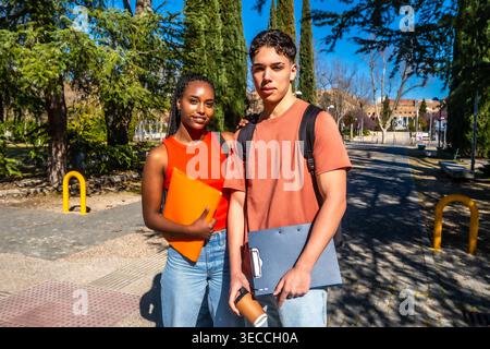 Diverse students carrying folders looking at camera on university campus Stock Photo