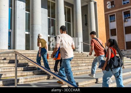 Diverse students walking up stairs on university campus Stock Photo