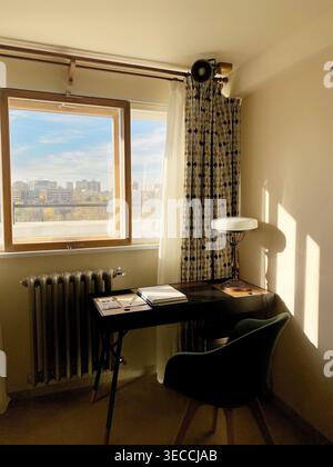 Cozy workspace by window with desk, chair and warm sunlight, minimal home office interior with city view and soft shadows Stock Photo