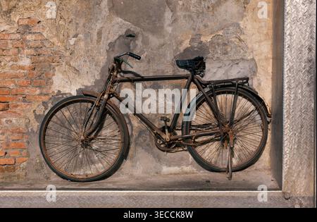 Rusty old bicycle leaning against a textured brick and concrete wall, showcasing its vintage charm and wear Stock Photo