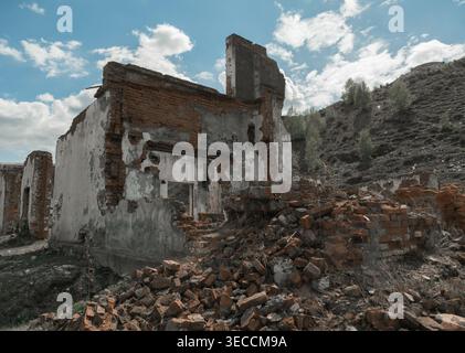 Old building in ruins with fallen bricks on the ground under cloudy sky in remote area Stock Photo