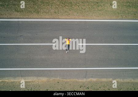Aerial view of a lone traveler rests on an empty straight road, enjoying quiet serenity with hands behind head Stock Photo