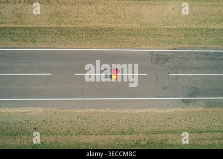 Aerial view of a couple travelers rest on an empty straight road, enjoying quiet serenity with hands behind head Stock Photo