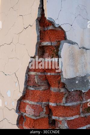 Damaged building wall reveals red brick structure beneath peeling and cracked exterior plaster Stock Photo