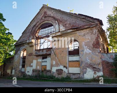 Historic brick building in ruins with broken arched windows and peeling facade against a clear sky Stock Photo