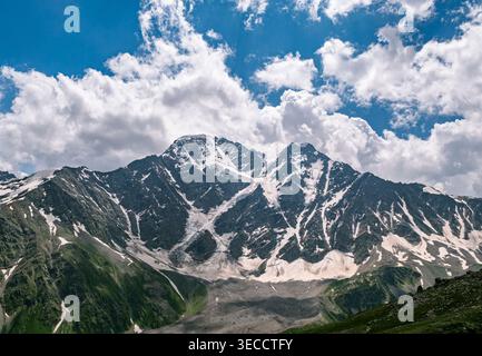 Majestic snow-capped mountain range under a vibrant blue sky with dramatic white clouds during summer Stock Photo