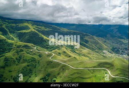 Panoramic view of verdant hills and valleys crossed by a winding road under a dramatic cloudy sky in a mountain range Stock Photo