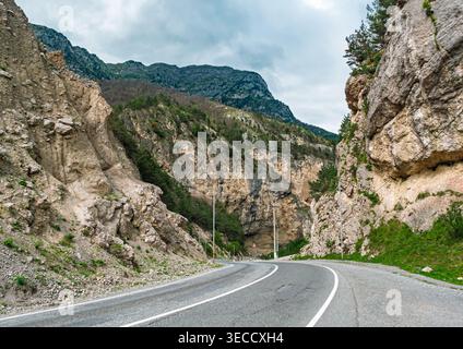 Scenic winding mountain road carves a path through a deep rocky gorge on a cloudy day Stock Photo