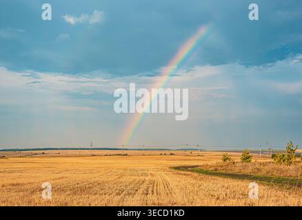 Bright rainbow arches over a golden field of harvested grain in rural countryside during daytime Stock Photo