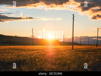 Radiant sunset over an expansive field with utility poles and rolling hills Stock Photo