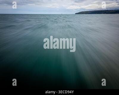 A high-speed motion blur effect over blue sea water moving towards a distant green coast and horizon. Concept of fast travel, marine journey, and velo Stock Photo