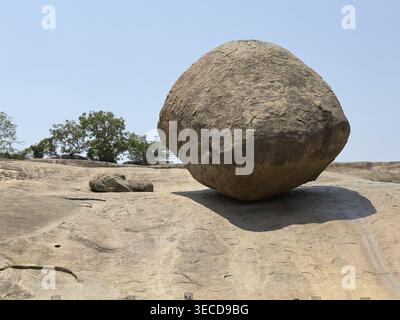 A massive round rock lies solitary on flat rocky ground under a clear sky, Krishna's butter ball, Mahabalipuram, Tamil Nadu, India Stock Photo