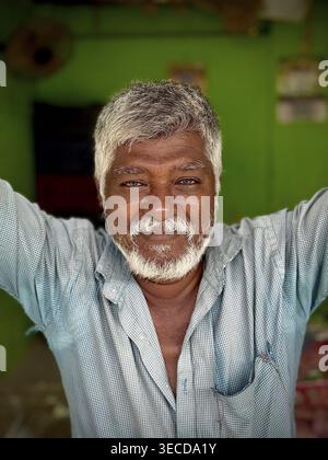 An elderly man with grey hair and beard smiles against a green background, India Stock Photo