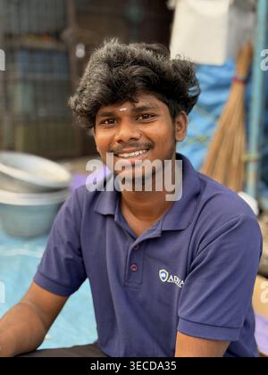 A young man wearing a blue polo shirt smiles friendly in a relaxed setting, India Stock Photo