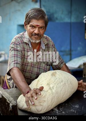 A man preparing traditional dough for paratha, in a checkered shirt, India Stock Photo