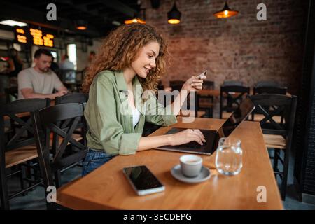 Smiling woman using laptop and credit card for online shopping in cafe Stock Photo