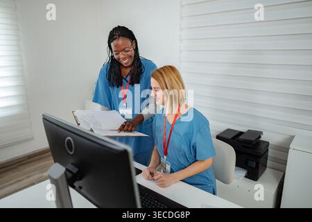 Two female nurses discussing patient information while working at a computer Stock Photo