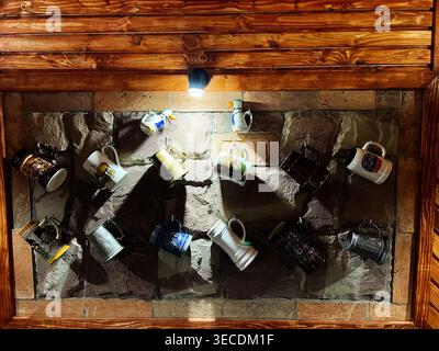 Rustic ceramic and metal mugs and beer steins displayed on a wooden wall with warm spotlight. Stock Photo