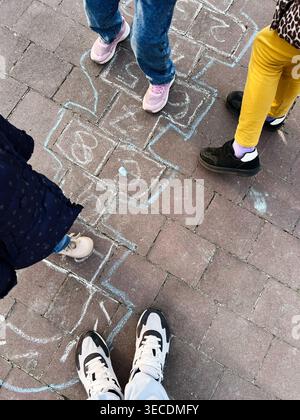Overhead view of kids playing hopscotch on pavement with chalk drawings and casual sneakers. Stock Photo