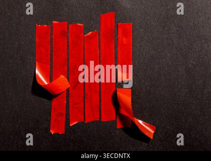 Red adhesive tape strips in a bar chart formation, some peeling off, sticking to a dark black textured surface Stock Photo