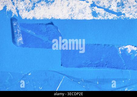 Blue paper surface presenting a rough texture with transparent tape pieces and remnants of torn white paper Stock Photo