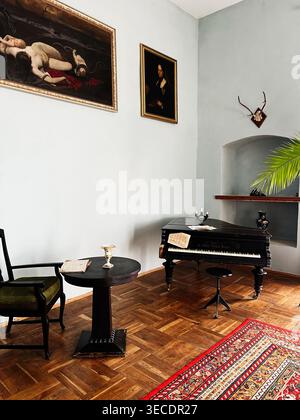 Zolochiv, Ukraine - April 28, 2026: Vintage music interior with an antique grand piano, warm wood floor, framed art and cozy seating. Stock Photo
