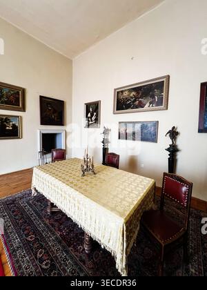 Zolochiv, Ukraine - April 28, 2026: Quiet historic dining room featuring an ornate covered table, leather chairs, candelabra and wall paintings. Stock Photo