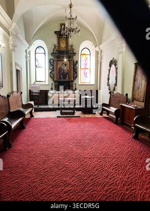 Zolochiv, Ukraine - April 28, 2026: Quiet historic chapel interior featuring an ornate altar flanked by stained glass windows and wooden pews. Stock Photo
