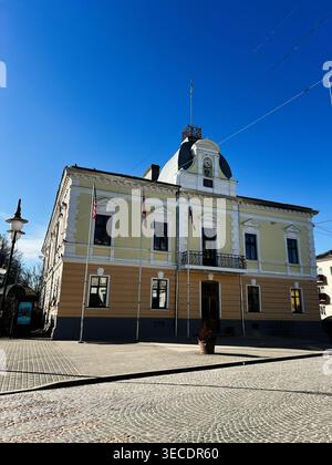 Zolochiv, Ukraine - April 28, 2026: Historic town hall facade with flags, balcony and cobblestone square bathed in clear sunlight. Stock Photo