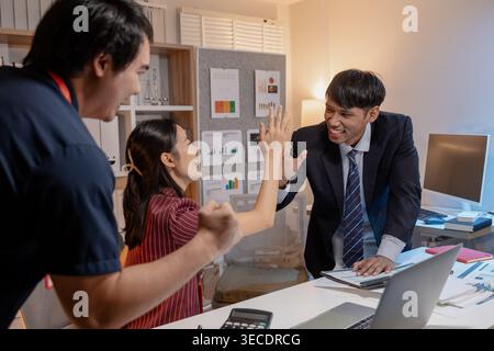 Business colleagues celebrating success in office, smiling and giving high five across desk, showing teamwork, achievement, and positive collaboration Stock Photo