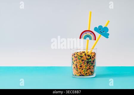 Colorful candy in glass with rainbow and cloud straws on pastel blue background. Minimal trendy candy concept. Original playful image with copy space. Stock Photo