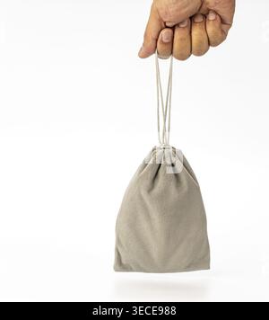 Close-up studio shot of a human hand holding a soft gray velvet drawstring pouch bag by its thin cord ties against a white background. Ideal for gift, Stock Photo