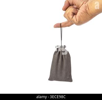A mature human hand pinches a dark twisted cord suspending a small gray velvet drawstring pouch bag in mid-air. Isolated on a clean white background, Stock Photo