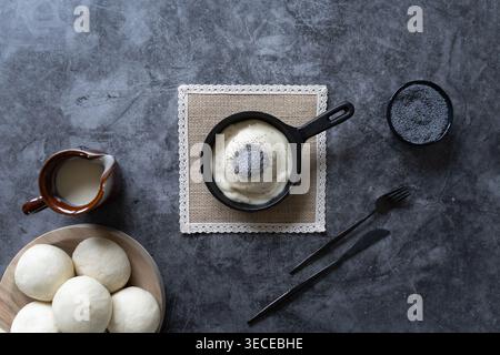 Overhead view of sweet dumpling with cream in pan with milk eggs and utensils on dark surface Stock Photo