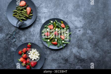 Overhead composition of two plates with arugula strawberry mozzarella salad on dark surface Stock Photo