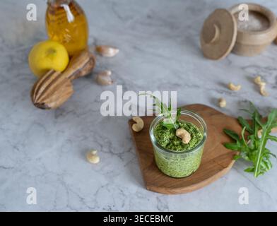 Front view of green pesto with cashews and arugula in glass with fresh ingredients on table Stock Photo