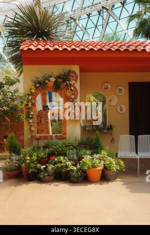 Mediterranean garden with terracotta roof and arch window in a conservatory, with potted herbs, wall plates, and a glass dome above. Stock Photo