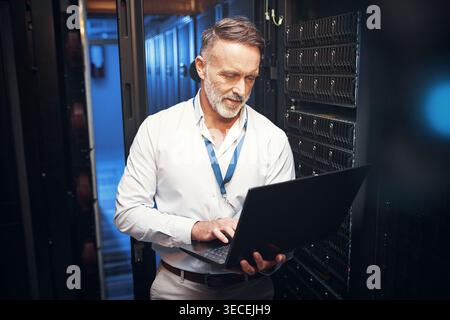 Smile, technician or typing on laptop in server room for cybersecurity, maintenance or database update. IT engineer, mature man and tech in data Stock Photo