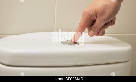 Close-up of male hand pushing a button to flush a close tool at home Stock Photo