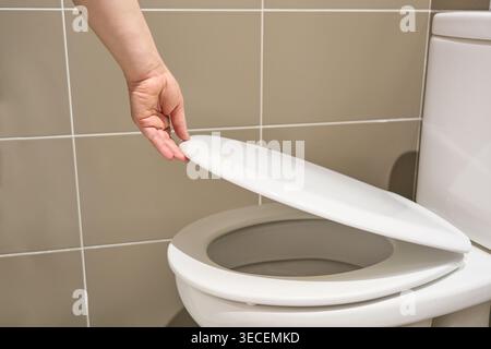 Scrubbing and cleaning. Shot of a hand closes or opens the toilet lid a bathroom toilet. Stock Photo