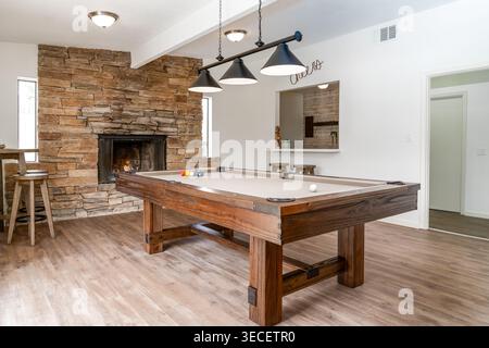 Rustic style solid wood pool table in spacious home game room with stone fireplace modern lighting stools bar Stock Photo