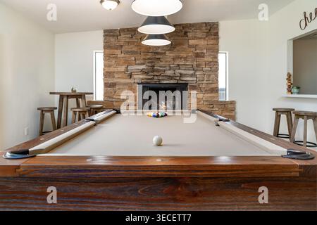 Rustic style solid wood pool table in spacious home game room with stone fireplace wooden bar stools tables Stock Photo