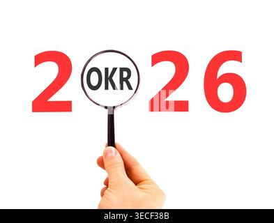 2026 OKR objectives and key results symbol. Concept words 2026 OKR in magnifying glass. Beautiful white background. Businessman's hand. Business 2026 Stock Photo