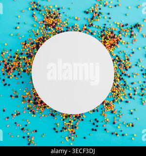 Colorful candy sprinkles frame with round paper card note copy space on pastel blue background. Creative trendy candy concept. Flat lay, top view. Stock Photo