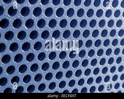 Close-up of shiny perforated metal surface with blurred background and patterned holes Stock Photo