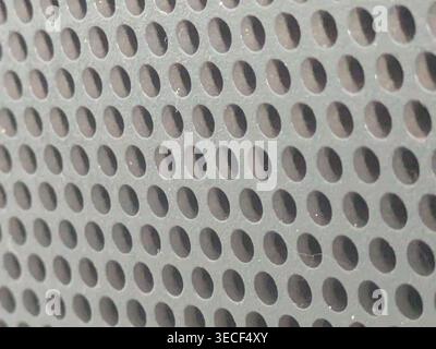 Close-up of shiny perforated metal surface with blurred background and patterned holes Stock Photo