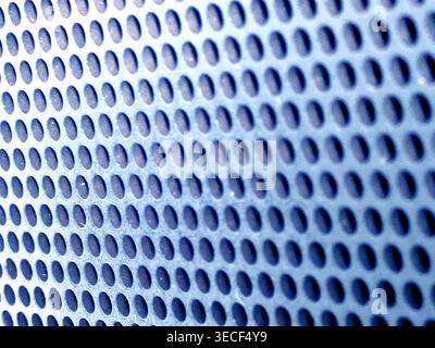Close-up of shiny perforated metal surface with blurred background and patterned holes Stock Photo